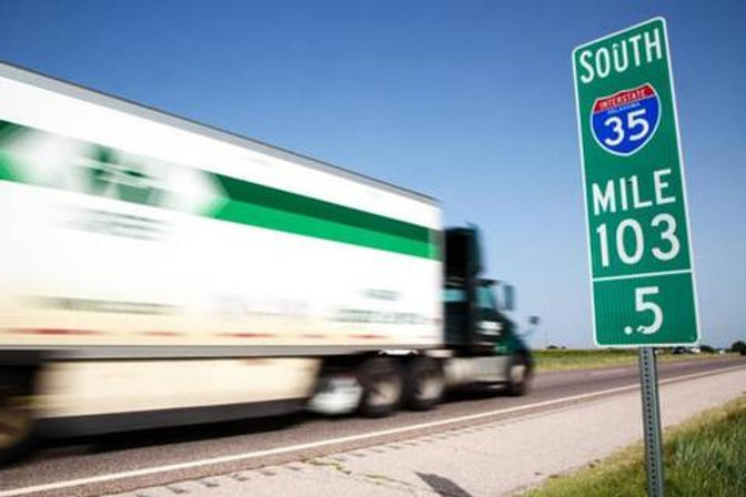 A tractor-trailer passing a green Interstate mile marker